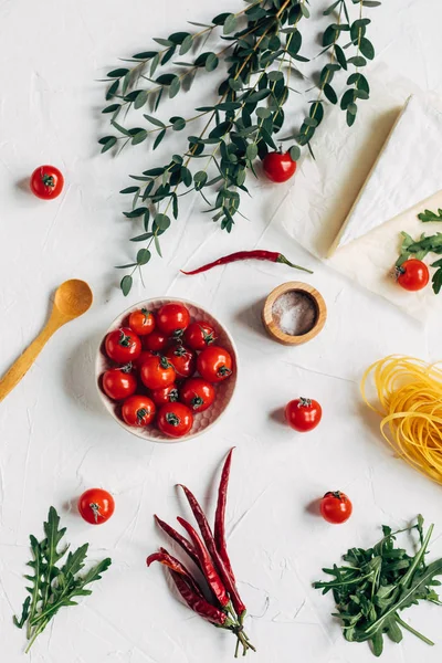 Served table with spaghetti, piece of cheese, chilli and cherry tomatoes in dish on white background