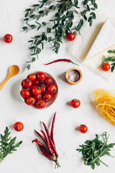 Served table with spaghetti, piece of cheese, chilli and cherry tomatoes in dish on white background