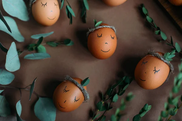 Easter composition with eggs with faces on craft paper background surrounded by green branches