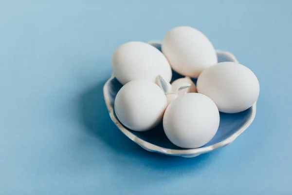 青色の背景に青色のセラミック プレートに白い卵をイースター組成 — ストック写真