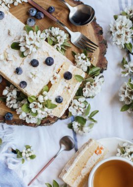 Taze böğürtlenli tatlı pasta ve ahşap tabakta bahar çiçekleri, bir fincan çay, üst manzara 