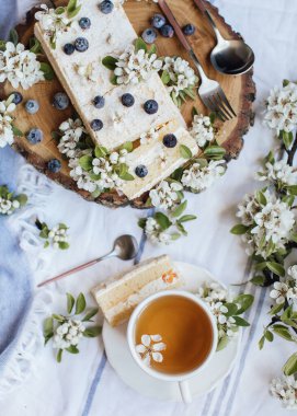 Taze böğürtlenli tatlı pasta ve ahşap tabakta bahar çiçekleri, bir fincan çay, üst manzara 