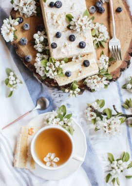 Taze böğürtlenli tatlı pasta ve ahşap tabakta bahar çiçekleri, bir fincan çay, üst manzara 