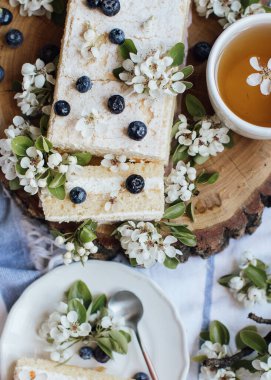 Taze böğürtlenli tatlı pasta ve ahşap tabakta bahar çiçekleri, bir fincan çay, üst manzara 