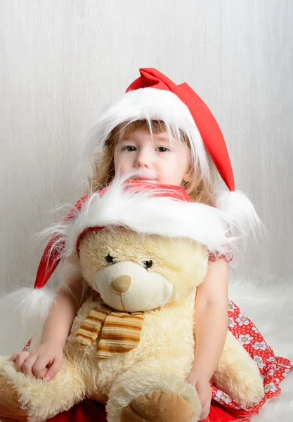 Klein meisje in kerstmuts met een teddybeer — Stockfoto