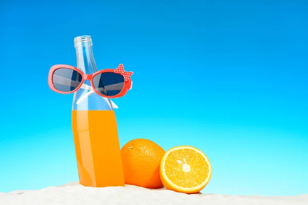 La botella de zumo de naranja y gafas de sol en la playa —  Fotos de Stock