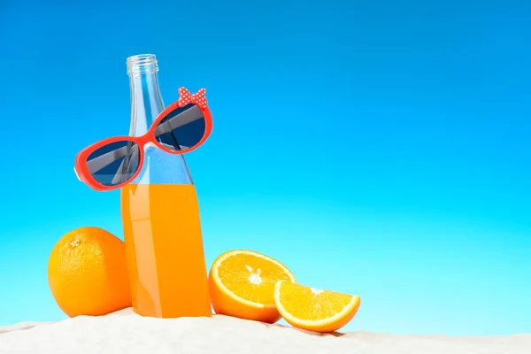 Бутылка апельсинового сока и солнцезащитные очки на пляже — стоковое фото