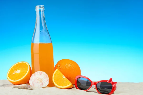 La botella de zumo de naranja y gafas de sol en la playa —  Fotos de Stock