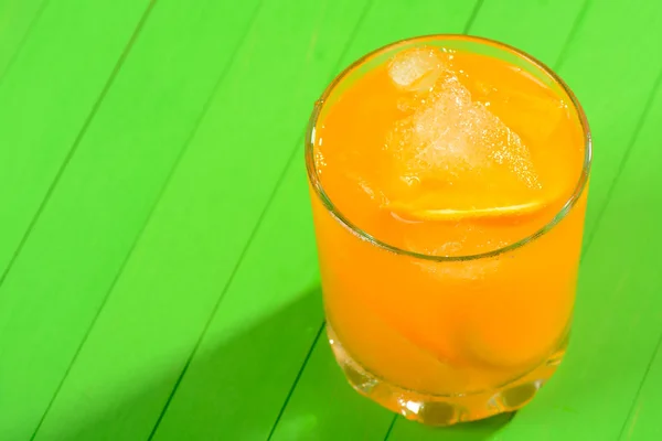 Un verre de jus d'orange glacé sur une table en bois vert — Photo
