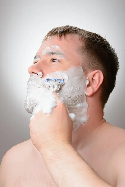 Um homem faz a barba em um fundo branco — Fotografia de Stock