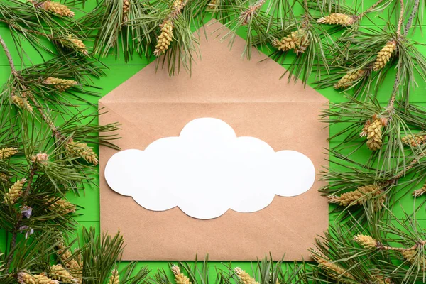 Ett tomt pappersark med ett kuvert bland tall grenar på en grön trä bakgrund — Stockfoto