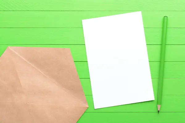 Ett tomt pappersark med ett kuvert på grön trä bakgrund — Stockfoto