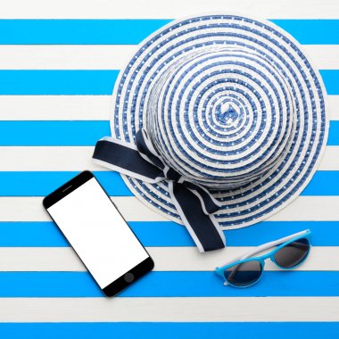 Çizgili şapka, güneş gözlüğü ve beyaz ve mavi arka plan üzerinde akıllı telefon. Üstten Görünüm, düz yatıyordu.