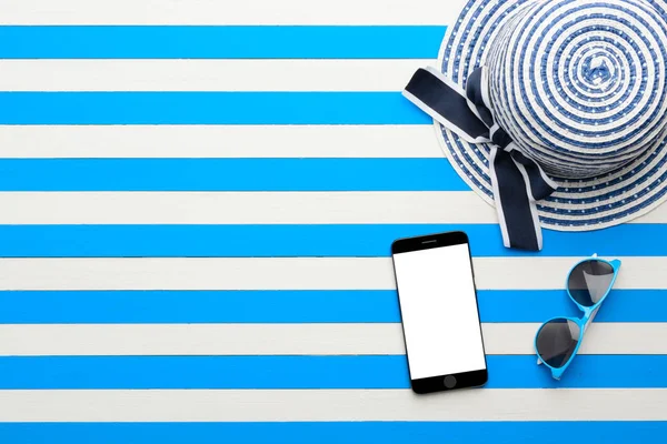 Çizgili şapka, güneş gözlüğü ve beyaz ve mavi arka plan üzerinde akıllı telefon. Üstten Görünüm, düz yatıyordu.