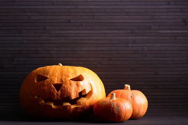 Halloween pompoen met eng gezicht en twee kleine pompoenen op de achtergrond van houten latten — Stockfoto