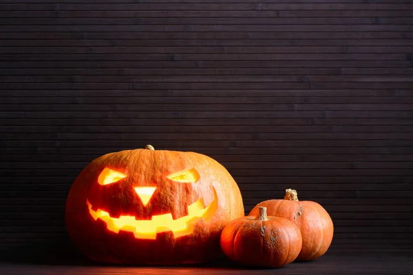 Halloween pompoen met enge gloeiend gezicht en twee kleine pompoenen op de achtergrond van houten latten — Stockfoto
