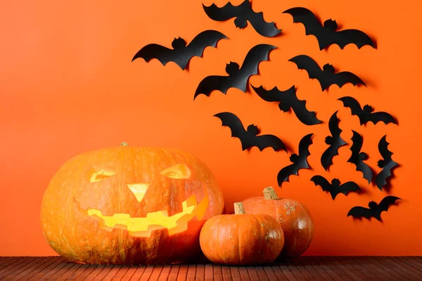 Parlayan Halloween pumpkins ve kağıt paketler bir turuncu duvar arka plan üzerinde yarasalar — Stok fotoğraf