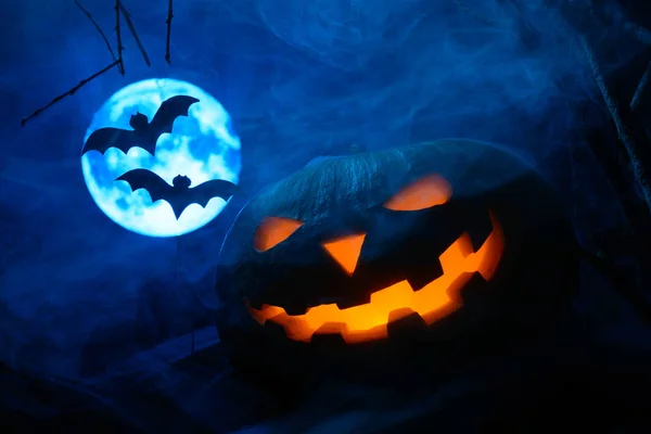 Strašidelné Halloween dýně s zářící tváří a netopýři na pozadí úplněk v mlze — Stock fotografie