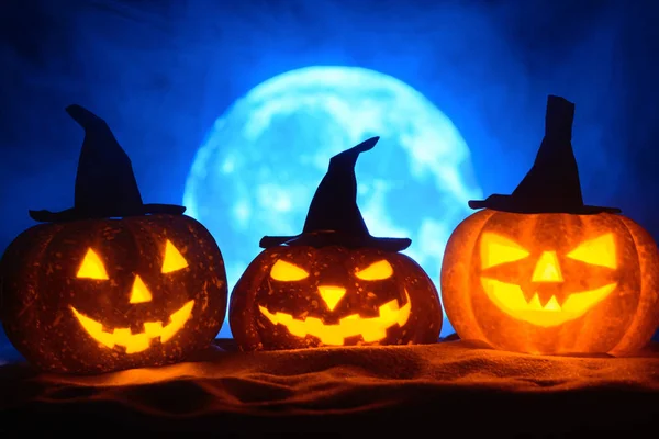 Tři Halloween dýně v čarodějnice klobouky na pozadí úplněk v mlze — Stock fotografie