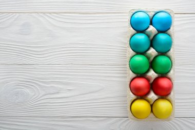 Bir tepsi ahşap beyaz bir arka plan üzerinde renkli Paskalya yumurta. Üstten Görünüm