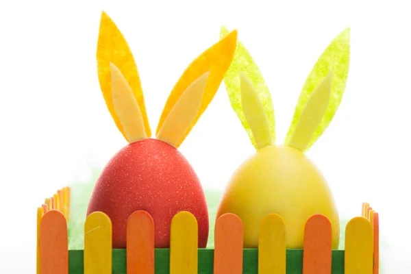 The composition of the eggs with the Bunny ears behind colorful fence — Stock Photo, Image