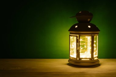 Tablo, yeşil zemin üzerine çelenk parlayan bir fener