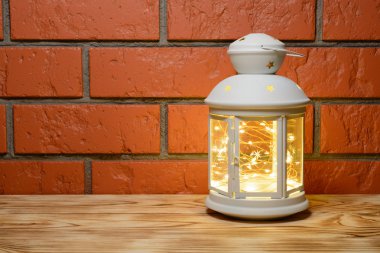 Ahşap masa, tuğla duvar arka plan üzerinde içinde çelenk parlayan bir fener