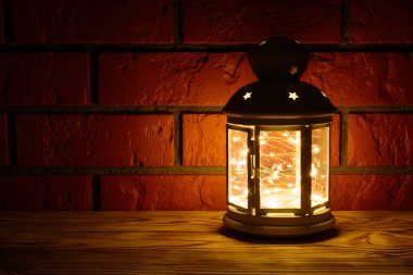 Ahşap masa, tuğla duvar arka plan üzerinde içinde çelenk parlayan bir fener