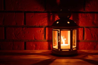 Bir fener ahşap masa, tuğla duvar arka plan üzerinde parlayan bir mum ile