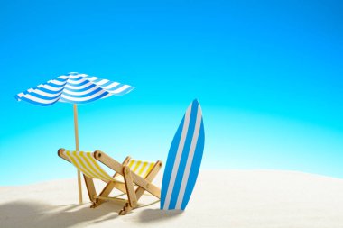 Şezlong şemsiye ve kumlu plajda sörf tahtası altında