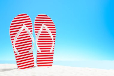 Kumlu bir plaj üzerinde kırmızı şeritli flip flop
