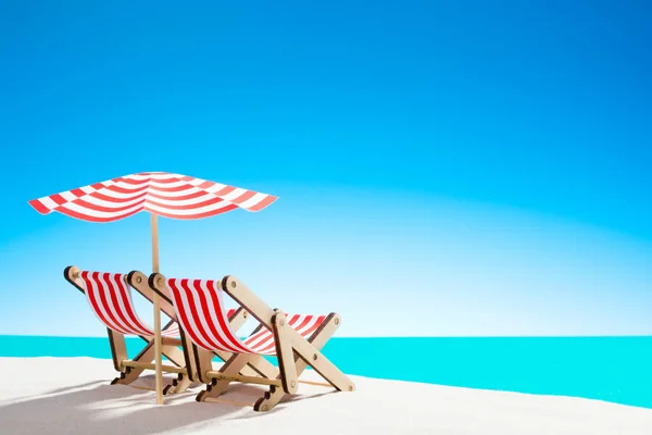 Two sun loungers under an umbrella on the sandy beach by the sea and the sky with copy space