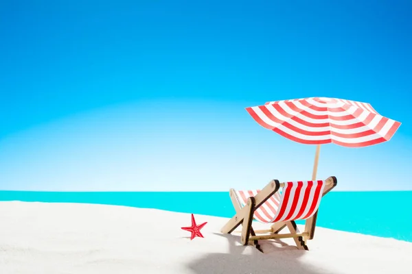 Una chaise longue bajo un paraguas en la playa de arena junto al mar y el cielo con espacio para copiar — Foto de Stock