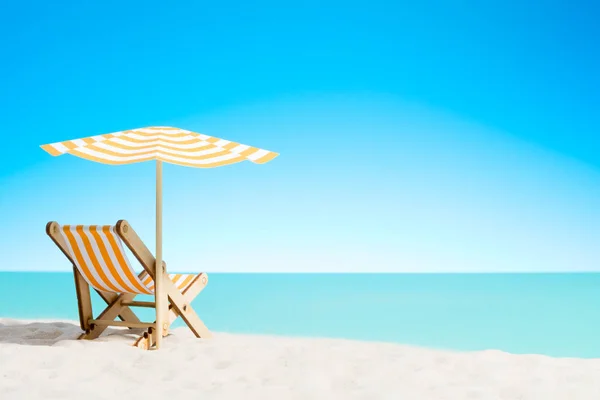 Una chaise longue bajo un paraguas en la playa de arena junto al mar y el cielo con espacio para copiar — Foto de Stock