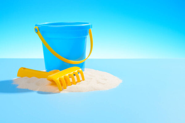 Игрушечное пластиковое ведро и грабли на песке. Синий фон с копировальным пространством
