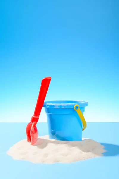 Játék műanyag vödör és a lapátot a homokba. Kék háttér-val másol hely — Stock Fotó