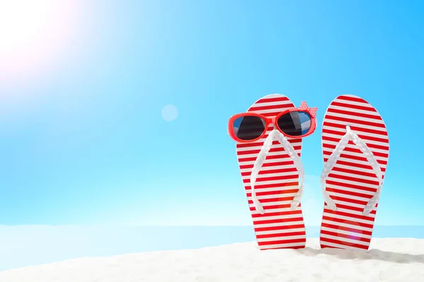 Red striped flip flops and sunglasses on sandy beach — Stock Photo, Image
