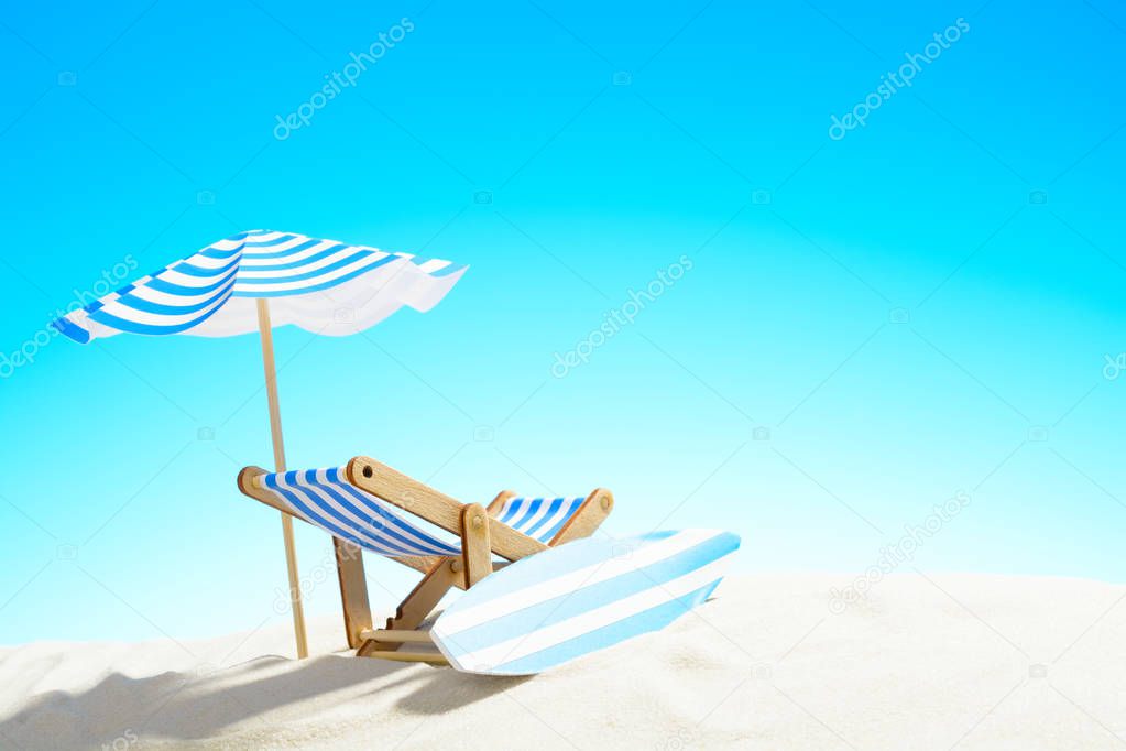 Deck chair under an umbrella and a surfboard on sandy beach