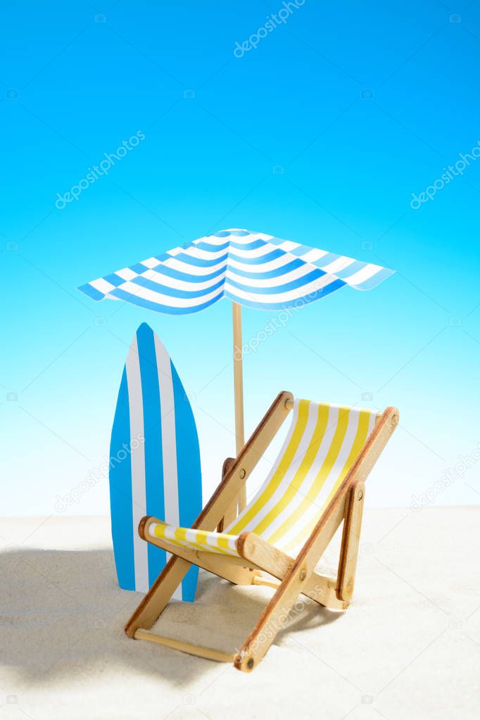 Deck chair under an umbrella and a surfboard on sandy beach