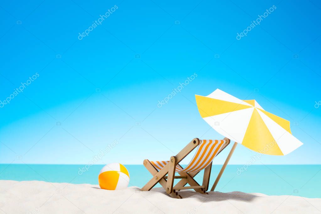 Lounge chair with parasol and beach ball on the coast