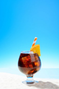 Buz ve kumlu sahilde bir cam turuncu bir dilim ile Cola yenileniyor