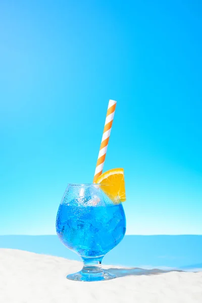 Освежающий голубой напиток со льдом и кусочек апельсина в стакане на песчаном побережье — стоковое фото