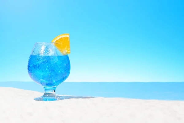 Orzeźwiający napój niebieski z lodem i plasterkiem pomarańczy w szklance na piaszczystej wybrzeżu — Zdjęcie stockowe