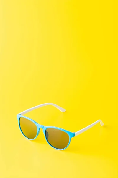 Un arreglo minimalista de gafas de sol azules sobre un fondo amarillo brillante —  Fotos de Stock