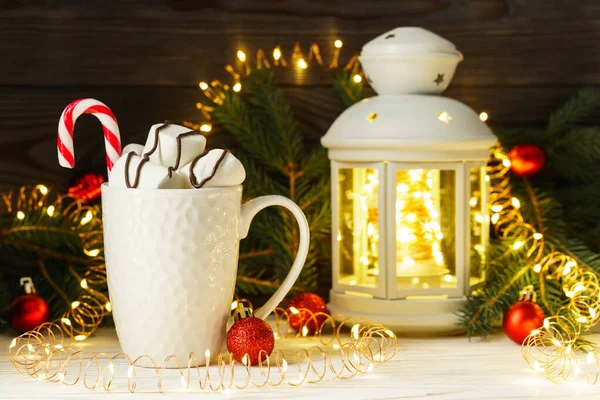 Guimauves douces et bonbons dans une tasse en céramique blanche près d'une lanterne de guirlandes sur une table en bois. Composition festive avec décorations de Noël et du Nouvel An . — Photo