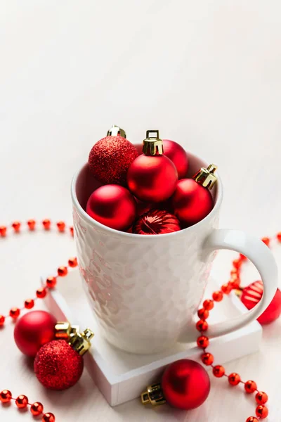 Boules décoratives de Noël rouges dans une tasse blanche. Table en bois blanc vue de dessus avec espace vide . — Photo