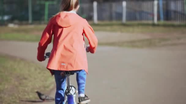 Teenager girl in a pink jacket rides a bicycle on a city street. — Stock Video