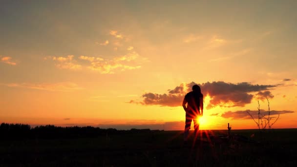 Un homme coiffé d'un casque soulève un vélo du sol. Silhouette d'un cycliste avec un vélo sur fond de coucher de soleil . — Video