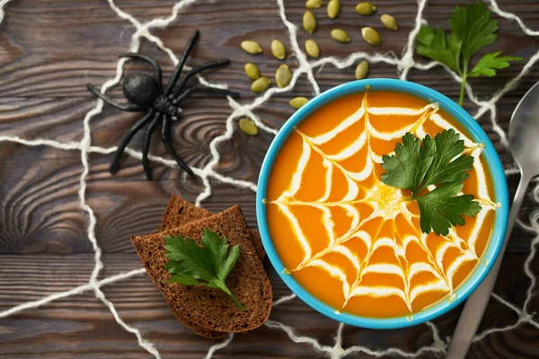 Krema ve maydanoz yapraklarıyla süslenmiş sağlıklı bir kabak püresi. Bayram için oyuncaklı güz kremi çorbası koyu ahşap arka planda Cadılar Bayramı, üst manzara.