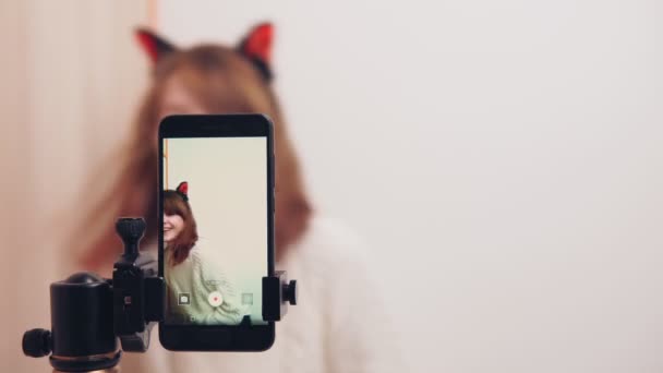 Une charmante fille heureuse inclut l'enregistrement vidéo dans un smartphone, une blogueuse Internet utilise son téléphone pour un blog vidéo sur les réseaux sociaux, salue les abonnés et parle en regardant la caméra . — Video